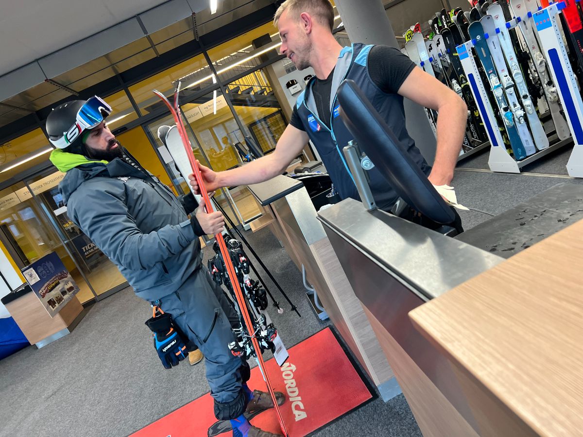 Rent and Go staff member handing skis to a customer at the rental shop; assistance and equipment selection.